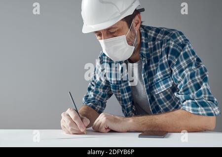 Project engineer with protective face mask writing notes on paper - performing calculations and writing specifications Stock Photo