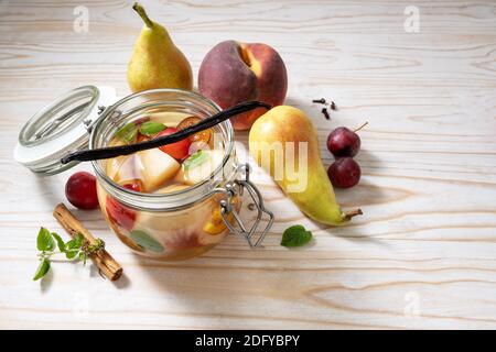 Preserving peach, pear and cherry plums with cinnamon, vanilla and mint in a glass jar to have canned fruits in winter, white painted rustic wood, cop Stock Photo