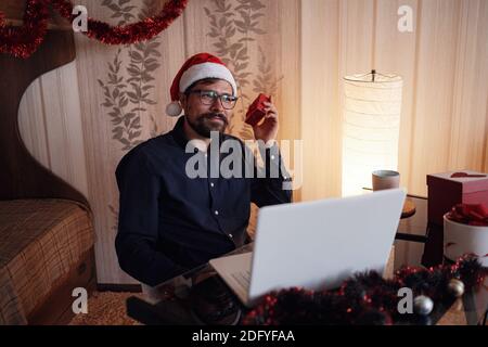 Virtual Christmas day house party. Man smiling wearing Santa hat Business video conferencing Online team meeting video conference calling from home. Stock Photo