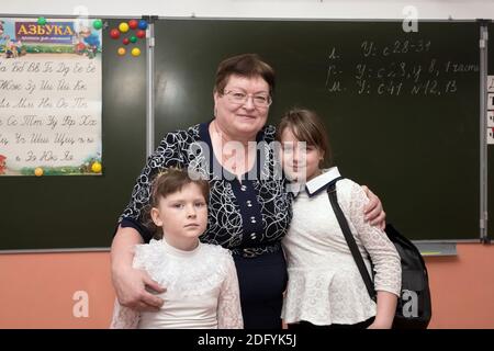 The teacher stands with the first-graders against the background of the blackboard with the Russian alphabet in the classroom. Stock Photo