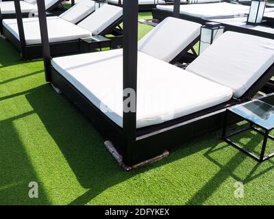 Empty white double sunbeds on green artificial grass on sunny day in summer. Stock Photo