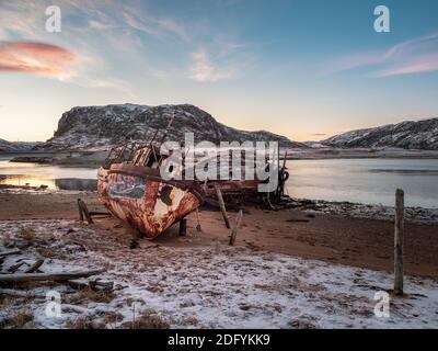 An old rusty fishing boat abandoned by a storm on the shore. Graveyard of ships, old fishing village on the shore of the Barents sea, the Kola Peninsu Stock Photo