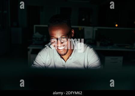 Successful smiling young african american businessman working overtime alone at his desk in an office late at night Stock Photo