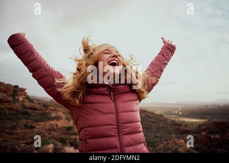 Cheerful young woman with hands raised and outstretched mountaineer with hair flying in wind enjoying fresh breeze - happiness and travel - achieving Stock Photo