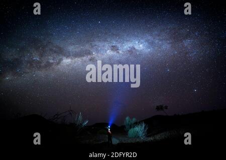 Person with light torch looking at the milky way in the Namibian desert, Damaraland, Namibia. Stock Photo