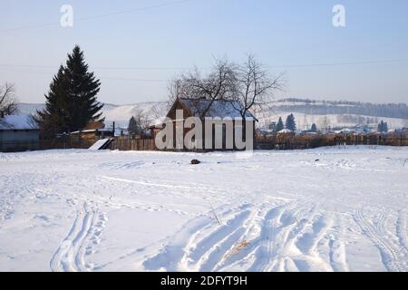 A wooden small house stands on a snowy hill in the village. Stock Photo