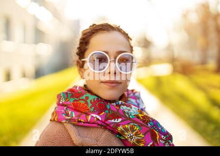 Portrait of young woman wearing warm coat, colorful scarf and sunglasses during winter Stock Photo
