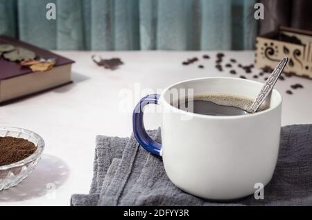 On the table on a napkin is a Cup of black coffee, next to coffee beans, ground coffee. Front view, close-up. Stock Photo