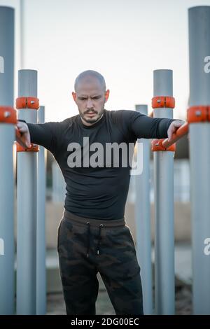 A young Hispanic man having a rest after exercising on the horizontal bars Stock Photo