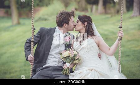 Bride and groom kissing on a swing bench, close up of wedding couple in vintage tone Stock Photo