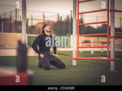 A young Hispanic man sitting on the grass and having a rest after working out Stock Photo