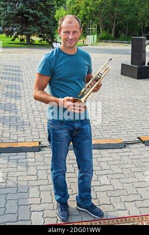 Young man stands in the square and holds a musical instrument - trumpet Stock Photo