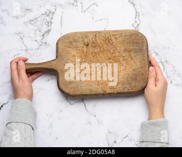 two female hands hold an empty old brown rectangular wooden cutting board, white background, top view Stock Photo