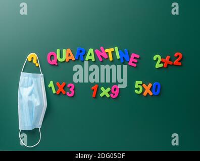 inscription quarantine from multi-colored plastic letter on a green chalk board, hanging disposable medical mask Stock Photo