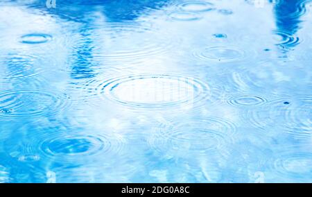 Stains circles on water from rain. Raindrops on pool blue water surface. blue water texture as background. Stock Photo