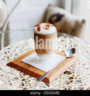 Hot latte or Cappuccino coffee on table in cafe or kitchen near the window.Morning coffee Latte with milk and chocolate on top in double walled glass Stock Photo