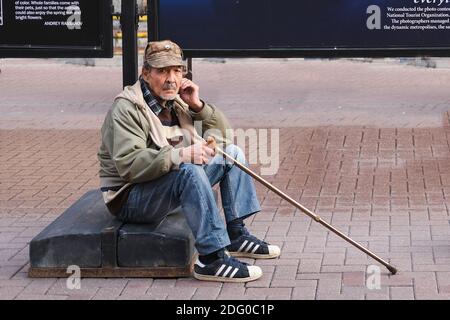 Frustrated Sad Elderly Man with stick sitting on street in solitude and looking at camera. Poverty and Despair, Social Pension Problems Stock Photo