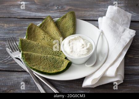 Spinach pancakes with cottage cheese sauce on a white plate on a wooden table. Delicious healthy breakfast Stock Photo