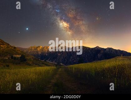 milky way over wheat field with rocky mountains in the background and a road in the center, very colorful Stock Photo