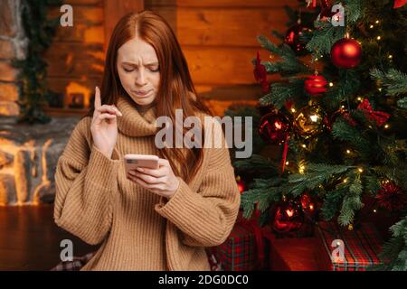 Close-up portrait of pensive redhead young woman typing online message using mobile phone. Stock Photo