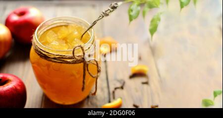 Apple jam in a transparent glass jar. Jam from apples and orange on a light background. Delicious marmalade. Stock Photo