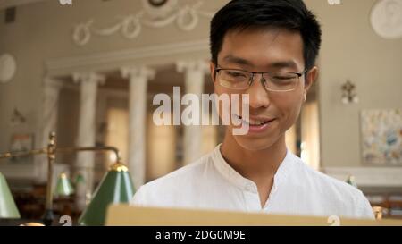 Portrait of smiling asian student happily opening envelope with exam results in university library. Young attractive guy studying in college Stock Photo