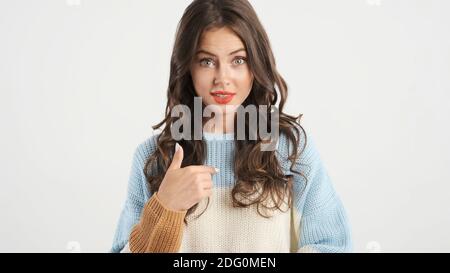 Beautiful girl in sweater pointing fingers on herself and amazedly looking in camera isolated Stock Photo