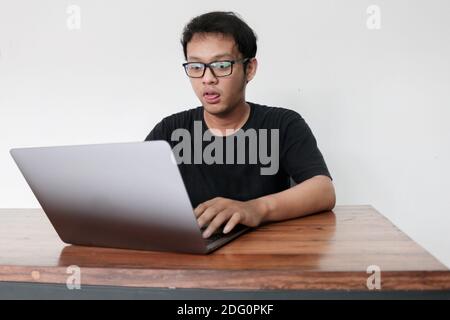 Young Asian man is boring and lazy in the front the laptop. Indonesia Man wear black shirt Isolated grey background. Stock Photo
