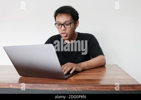 Young Asian man is boring and lazy in the front the laptop. Indonesia Man wear black shirt Isolated grey background. Stock Photo