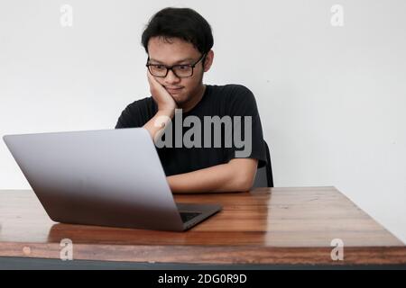 Young Asian man is boring and lazy in the front the laptop. Indonesia Man wear black shirt Isolated grey background. Stock Photo