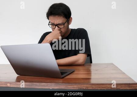 Young Asian man is boring and lazy in the front the laptop. Indonesia Man wear black shirt Isolated grey background. Stock Photo
