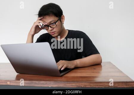Young Asian man is boring and lazy in the front the laptop. Indonesia Man wear black shirt Isolated grey background. Stock Photo