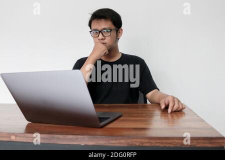 Young Asian man is boring and lazy in the front the laptop. Indonesia Man wear black shirt Isolated grey background. Stock Photo