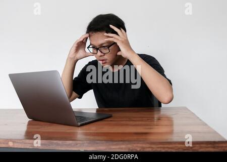 Young Asian man is boring and lazy in the front the laptop. Indonesia Man wear black shirt Isolated grey background. Stock Photo