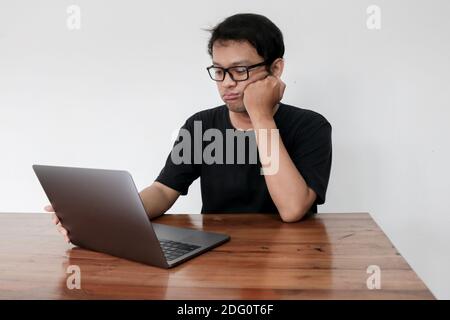 Young Asian man is boring and lazy in the front the laptop. Indonesia Man wear black shirt Isolated grey background. Stock Photo