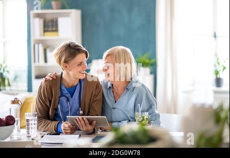 Senior woman with caregiver or healthcare worker indoors, using tablet. Stock Photo