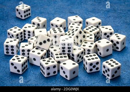 pile of white cubic dice with black pips (dots) against blue handmade paper, game, gamble, chance and risk concept Stock Photo