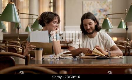 Attractive smiling students happily opening exam results in library. Young casual students studying together in college Stock Photo