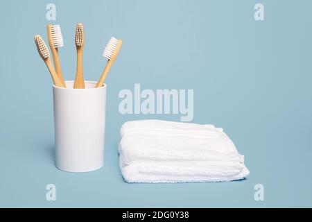 Four natural wooden bamboo toothbrushes in a white cup next to a white cloth on a blue background with copy space and room for text Stock Photo