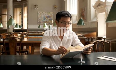 Young asian male student intently studying with textbook and preparing for exams in library Stock Photo