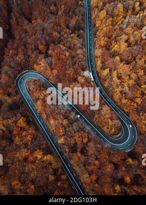 Aerial view of countryside road passing through the colorful autumn forest and mountain Stock Photo