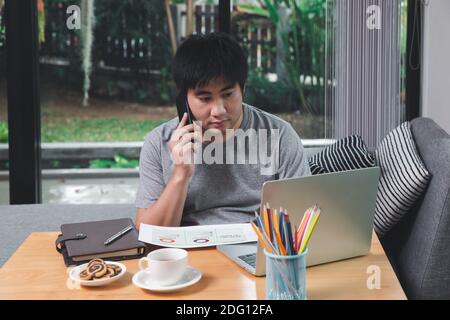 A man in casual wear using phone and working at home office. Stock Photo