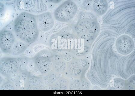 An aerial drone looking down captures patterns, shapes, holes and cracks in frozen lake ice. Stock Photo