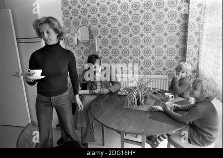 1970s England, a middle income professional couple at home with their two children. In the kitchen, mother making afternoon tea, sandwiches for the two boys, and a cup of tea for her husband who is reading the newspaper and paying no attention at all or interest in his children. He is bored family life. 1977 New town modern housing development Milton Keynes Buckinghamshire UK HOMER SYKES Stock Photo