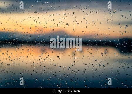 Close up of raindrops on a window with a sunset across water in the background Stock Photo