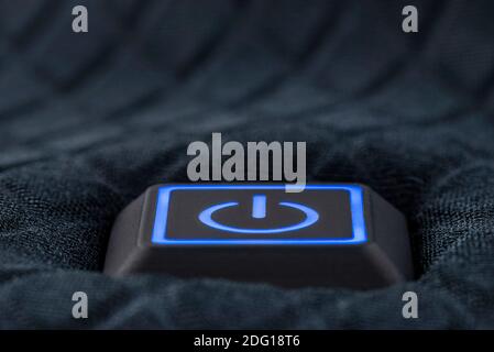 Macro shot of a plastic button with a blue power symbol, sewn into modern clothing. Stock Photo