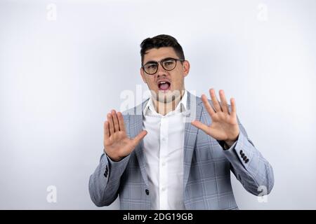 Business young man wearing suit over white background afraid and terrified with fear expression stop gesture with hands, shouting in shock. Panic conc Stock Photo