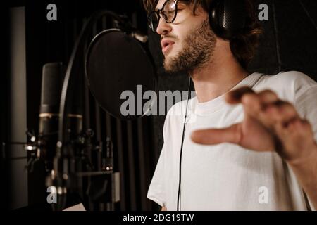 Close up young handsome male singer in headphones with professional microphone singing in recording studio Stock Photo