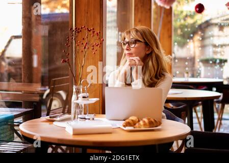 Confident mature woman deep in thought while working on laptop in cafe. Small business. Stock Photo