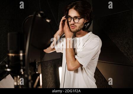 Young male singer wearing headphones preparing recording new song in sound studio Stock Photo
